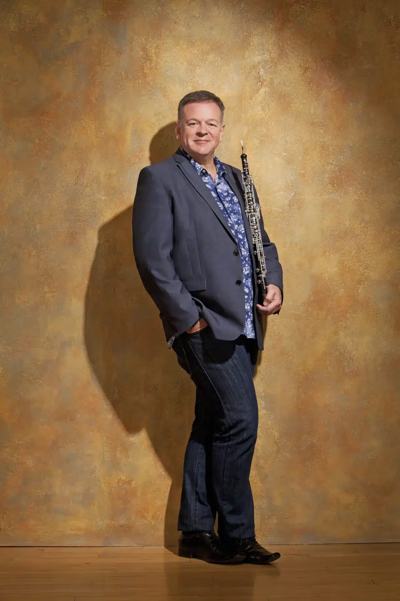 Portrait photo of Nicholas Daniel holding his oboe in from of a textured, yellow background