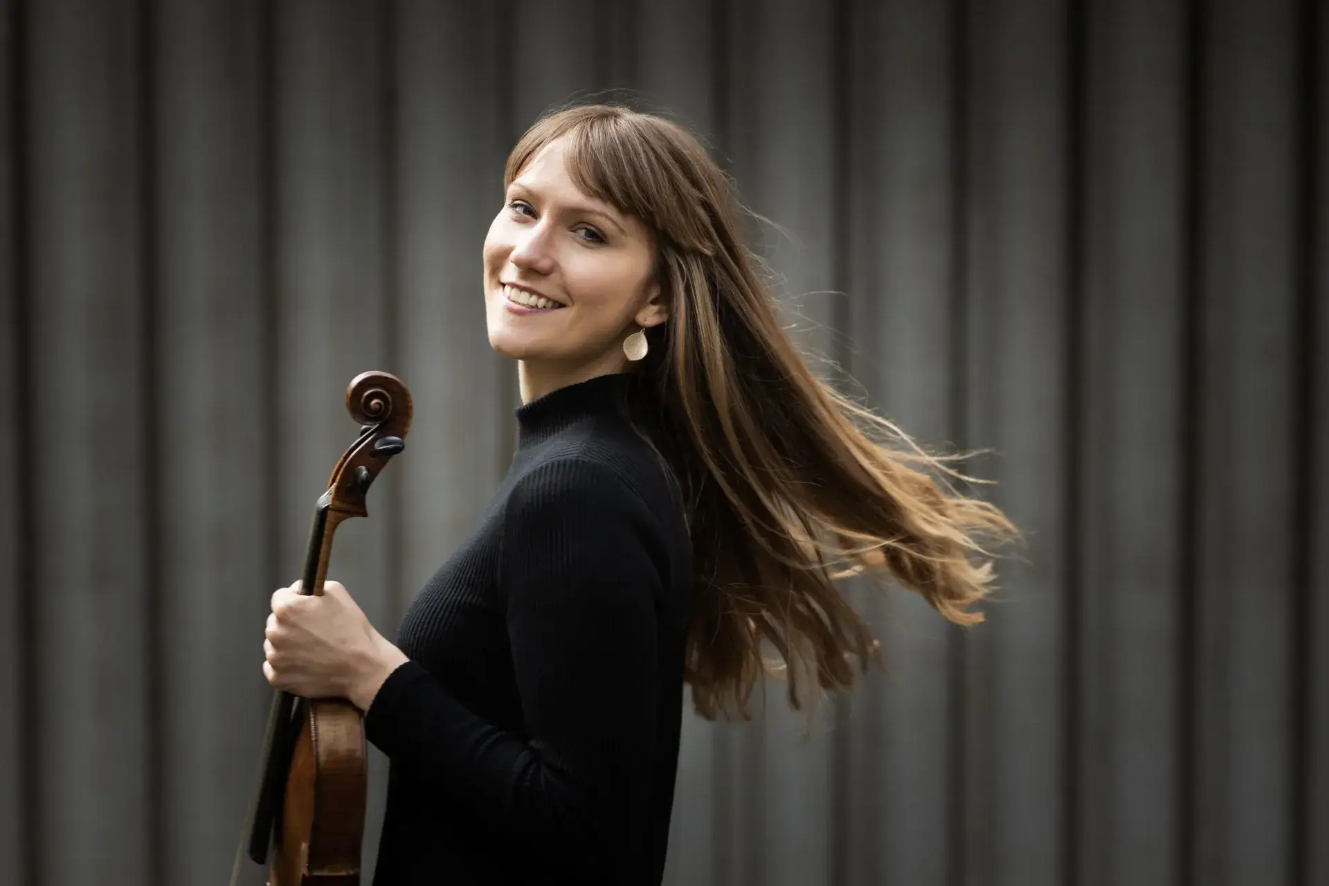 Portrait photo of Rosalind Ventris holding her violin and smiling